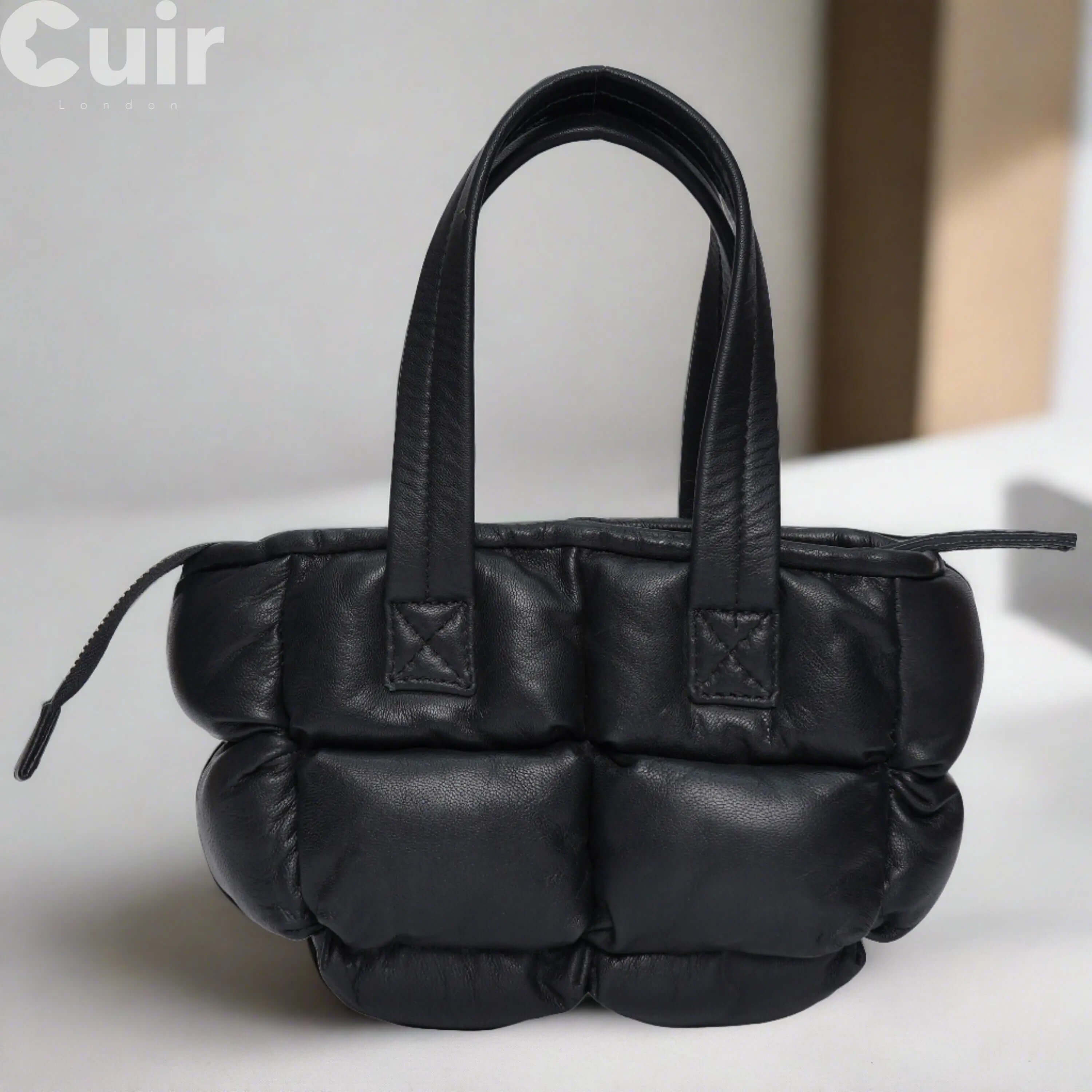 Black quilted mini leather handbag with dual handles and zipper closure.