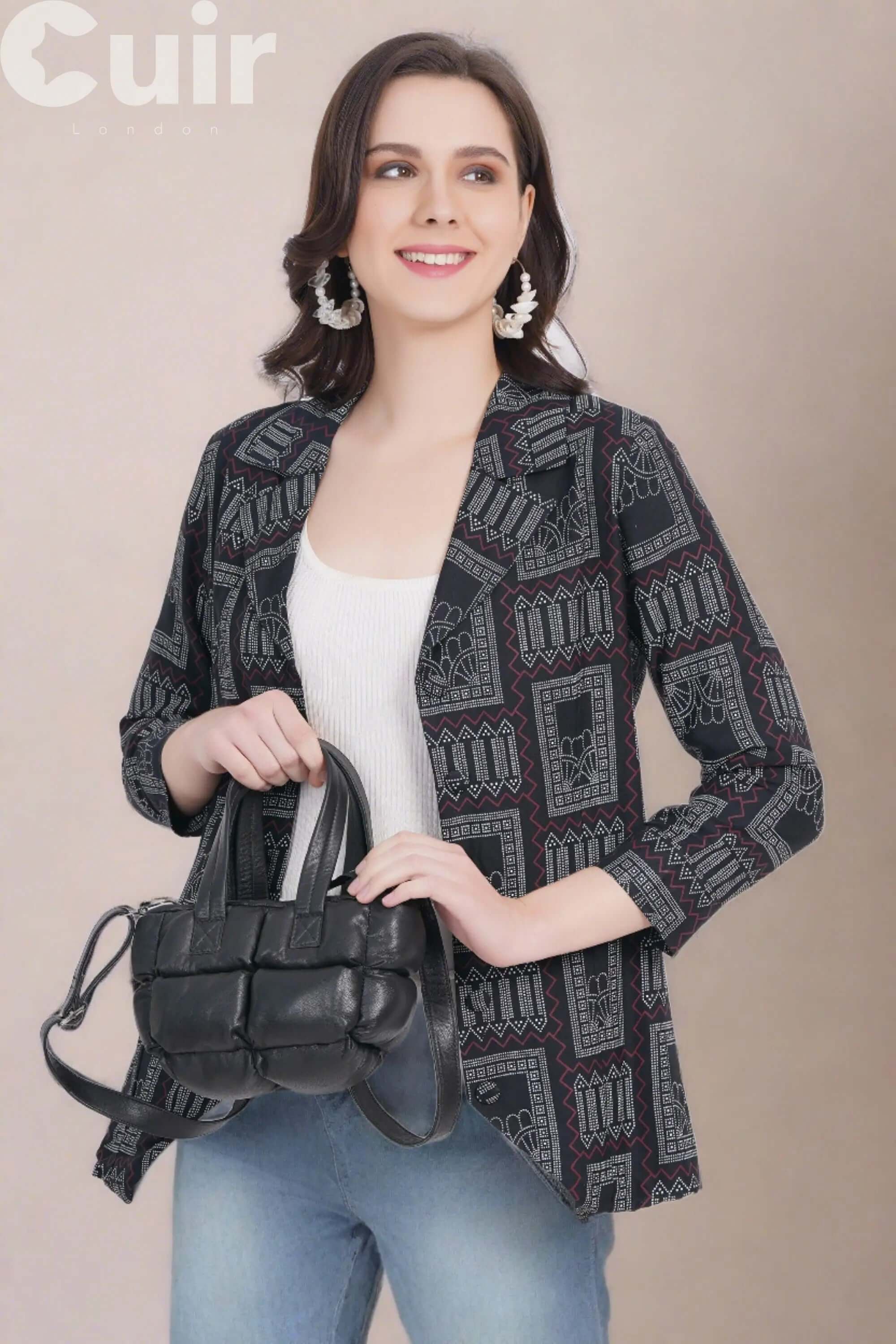 Woman holding black genuine leather crossbody bag wearing patterned blazer and jeans.